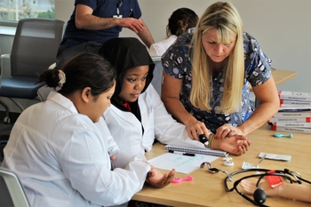 students in white coats at table with woman teaching