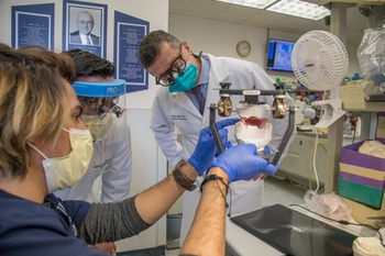Two people in lab coats look intently at a device being held by a third person.