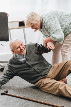 Older man on ground after fall and woman helps to get him up.