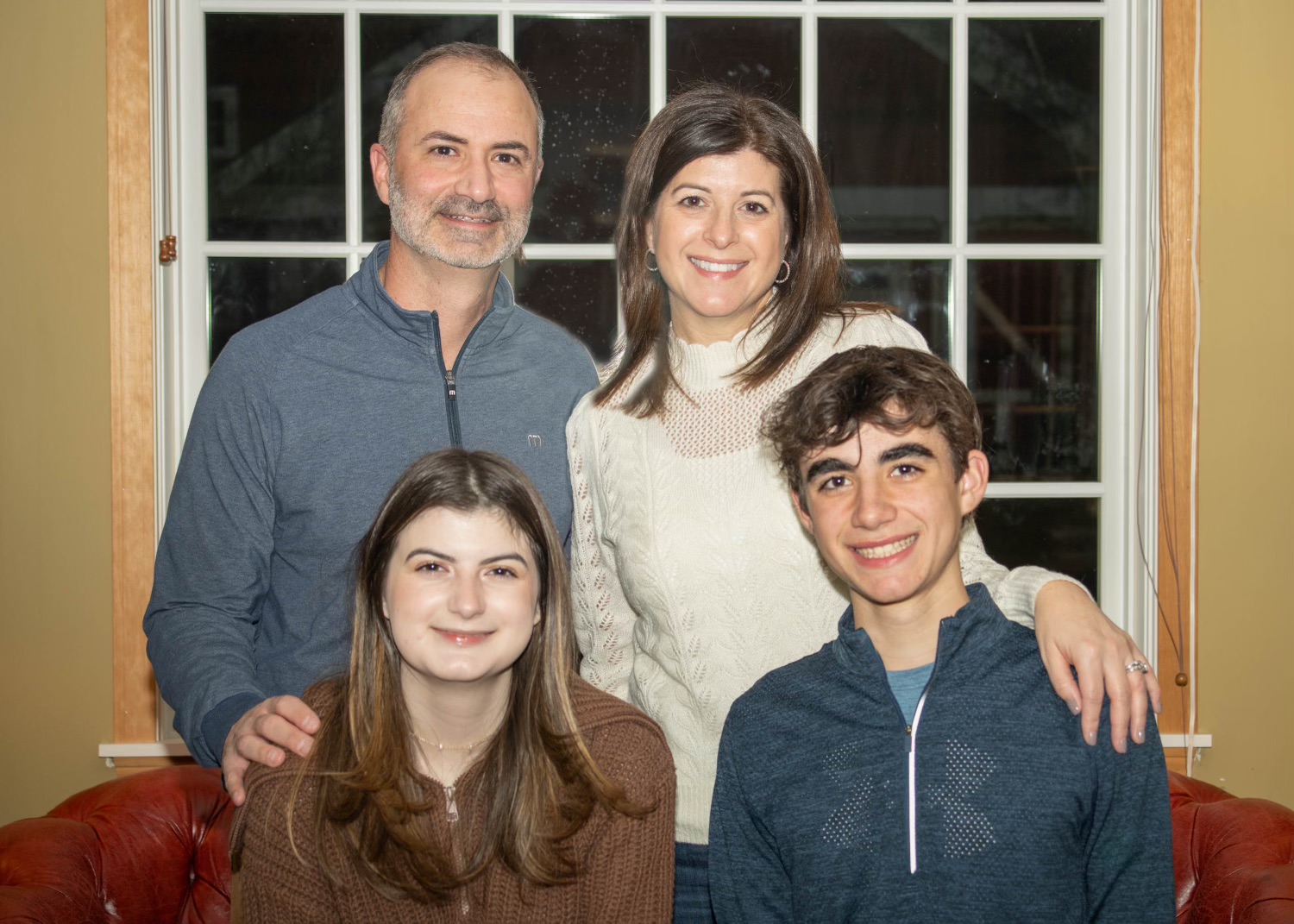 A family of four poses for a photo in a cozy living room. Father, Mother, Daughter and Son.