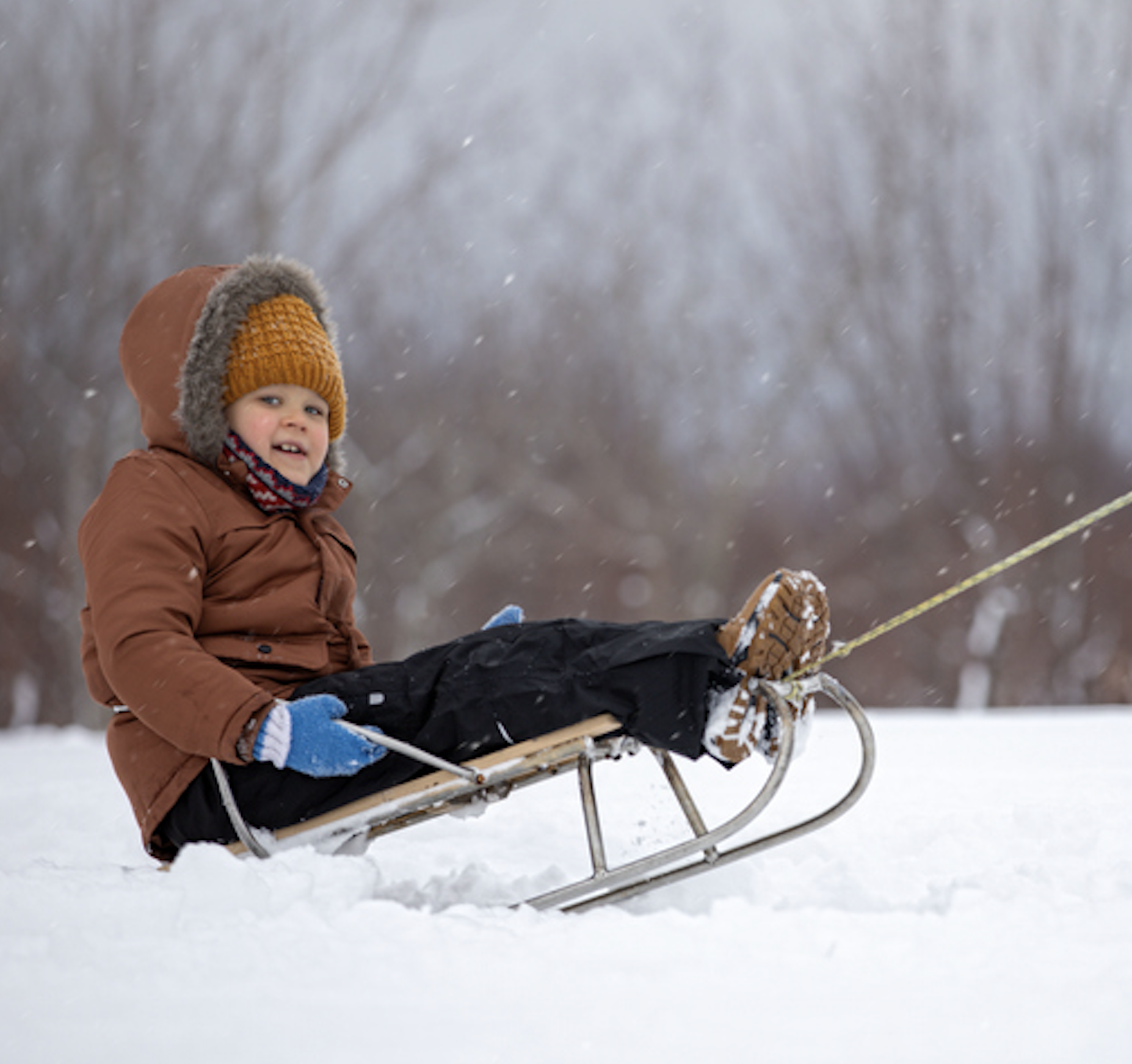 Toddler smiling while being pulled on a sled in the snow