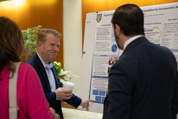 Tait Shanafelt, MD, gestures to a poster with information on the Wellbeing Fellow's project as attendees look on. 