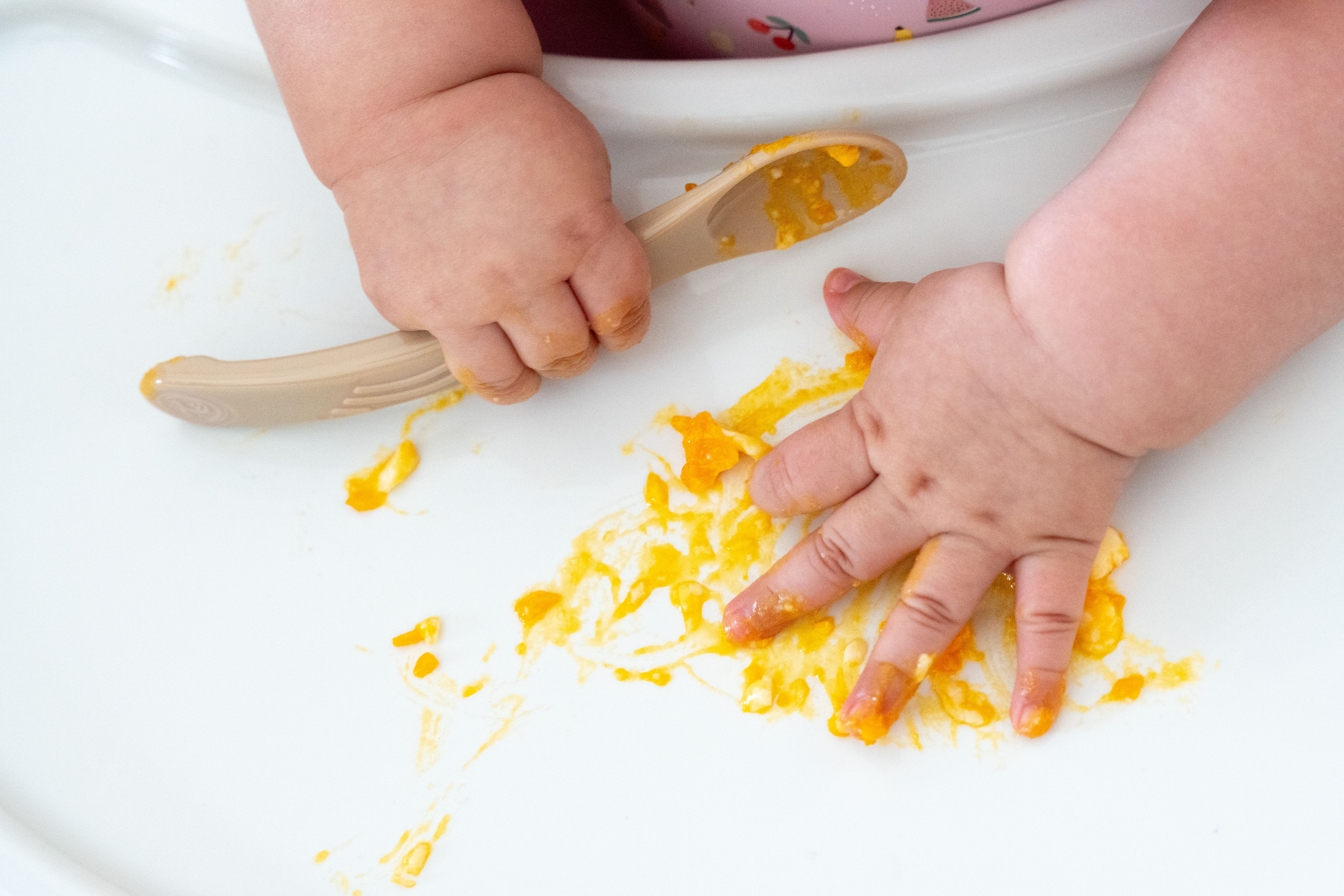 baby hands touching scrambled egg, also holding a spoon