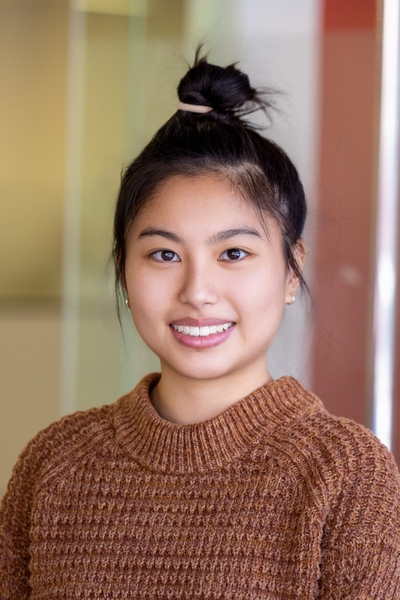 Yue Guzhang, hair in bun, brown sweater, smiling in head and shoulders portrait