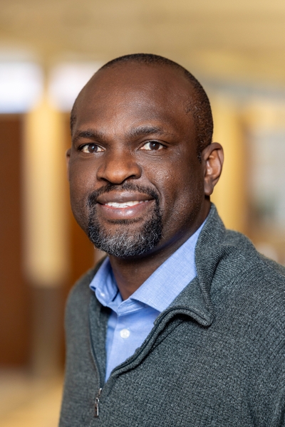 John Onukwufor, PhD, smiling looking at camera, wearing a grey sweater and blue button up shirt