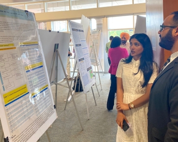 a woman in a dress explains a scientific poster to onlookers