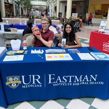 a man and a woman sit behind an informational table that says "Eastman Institute for Oral Health". The holds up a model of a mouth.