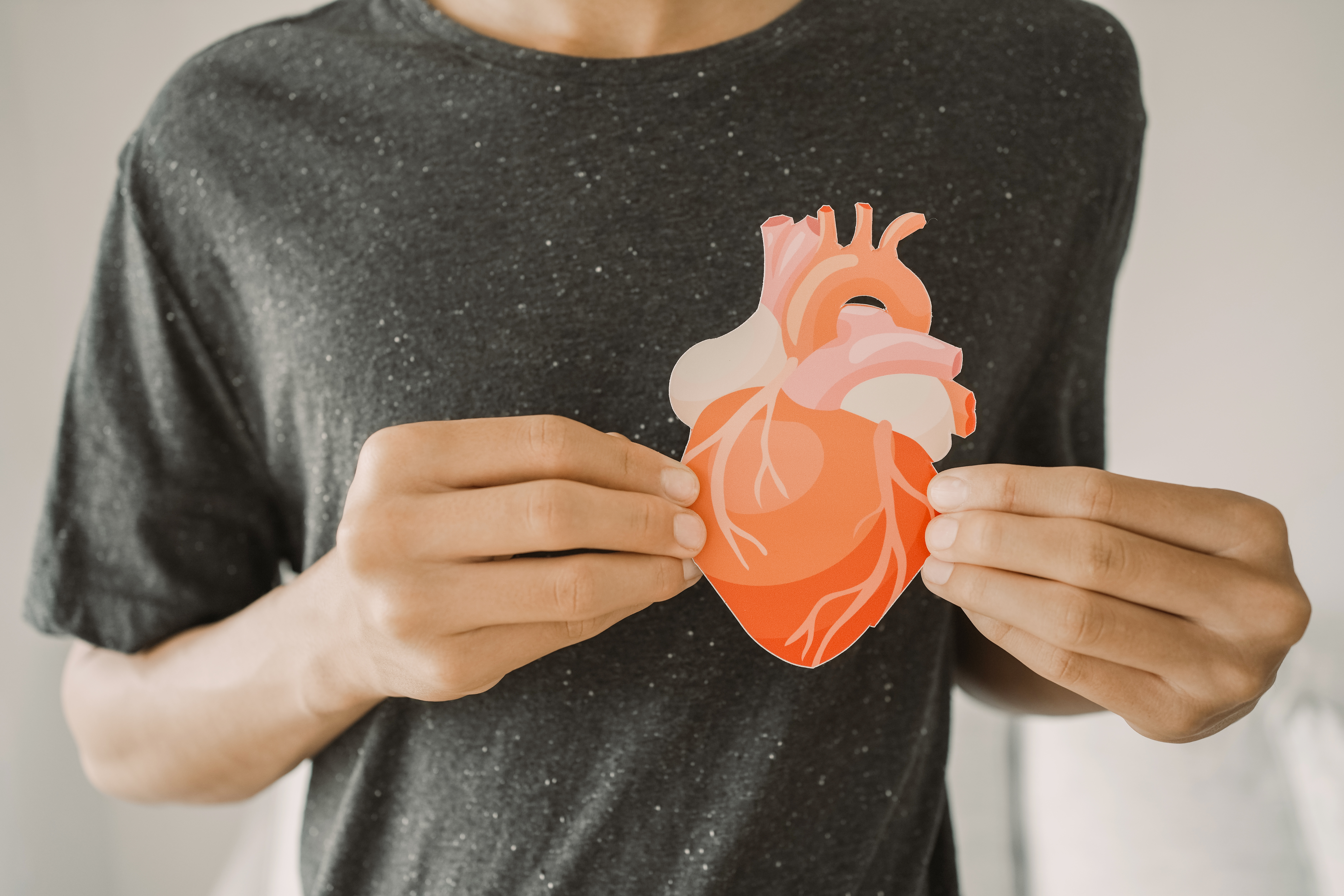 A teenager holds a cut out of a heart in front of his chest