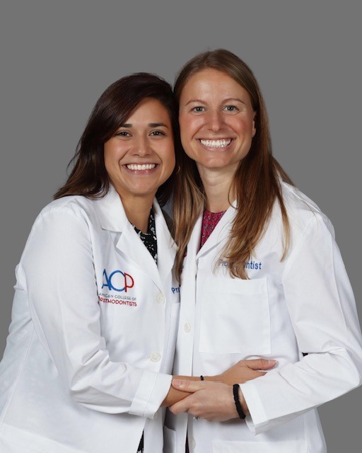 Two girls in white lab coats hug and pose together.