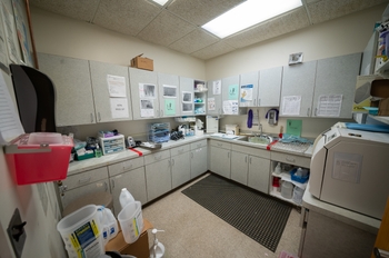 a sterilization room with a sink in well-worn cabinets. Sterilizer machines sit on the counter. Boxes are stacked on the left side by the wall.