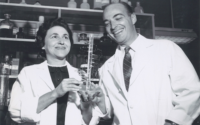 The Kornbergs laugh together while holding a model of DNA