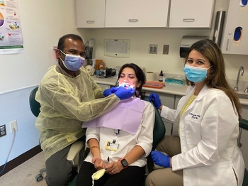 Dr. Altuhafy and a resident wear masks while treating a patient in a dental chair.