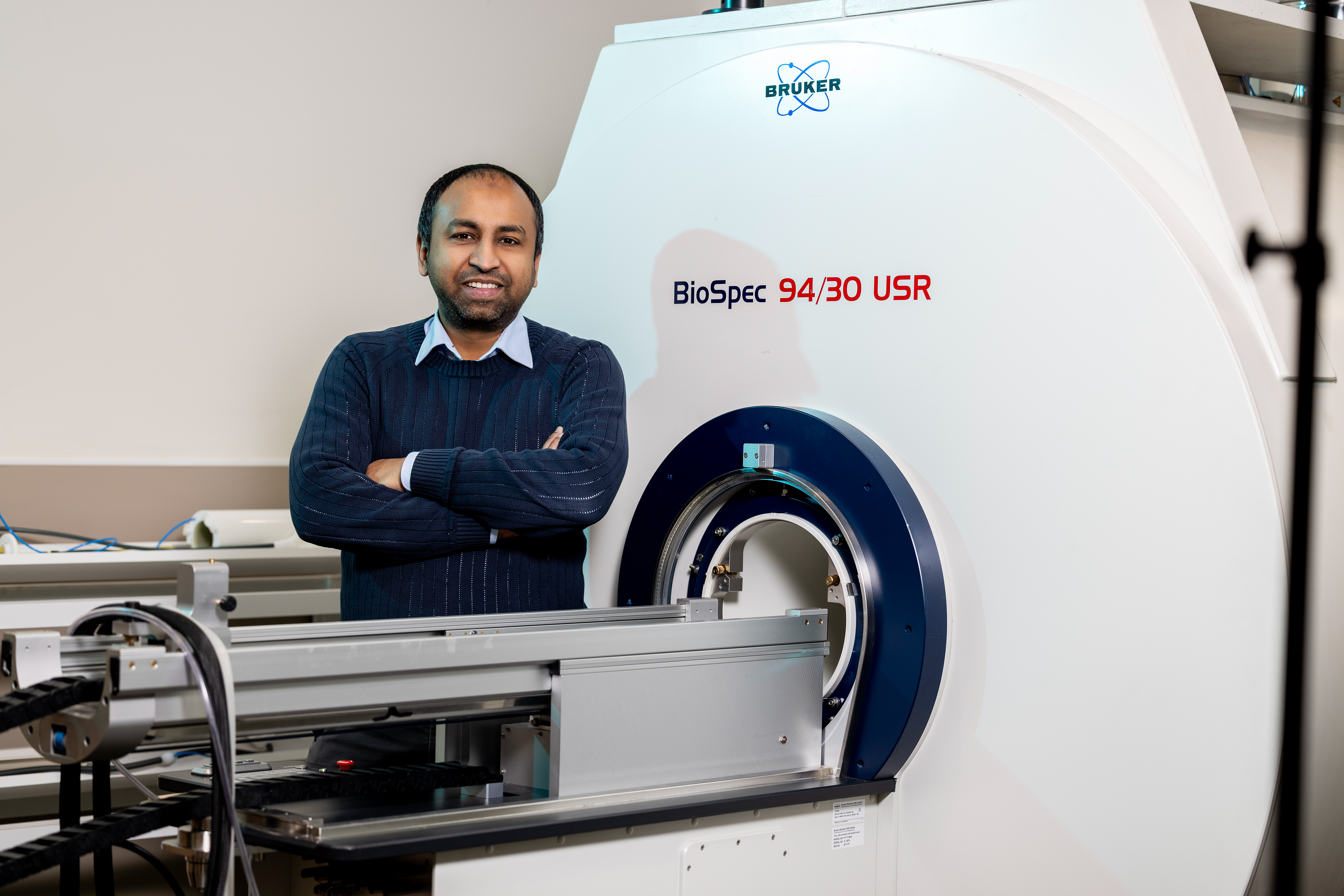 Man stands with arms crossed next to research MRI machine