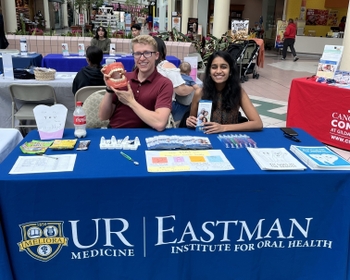 Two people sit behind an informational EIOH table in a mall, smiling warmly.