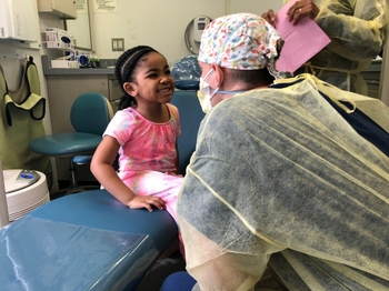 A young patient smiles up at a dentist, sitting in a chair on the smilemobile.