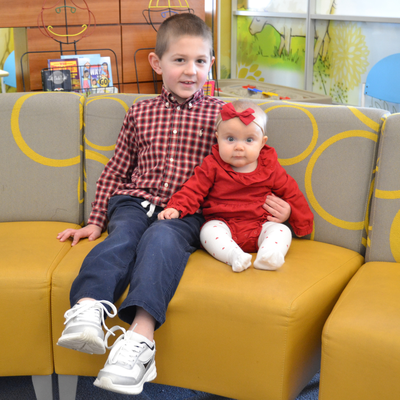 two children sitting next to each other on a couch, one six and one a baby. 