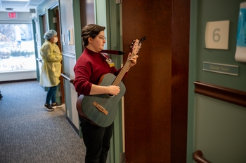 A woman plays a guitar as she enters a treatment room in a dental clinic.