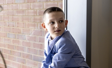young boy in blue suit sitting by window