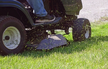 riding lawnmower with fresh grass clippings in the air nearby