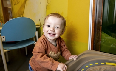 toddler standing at toy smiling at camera