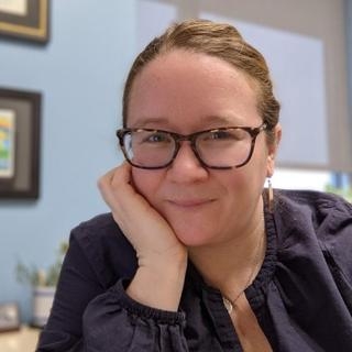Person wearing glasses with head in hand smiling at camera