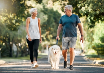 Man and woman walking outside with a dog in between them