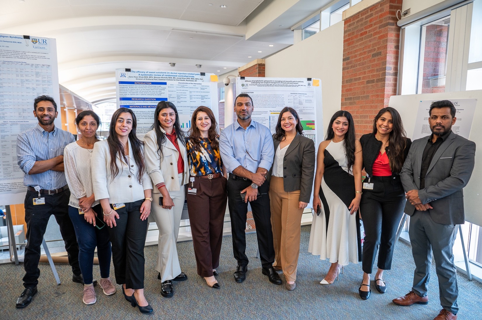A group of people in semi-formal attire stand together in front of four scientific posters.