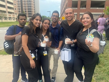 Six young adults stand together on the sidewalk smiling and holding ice cream.