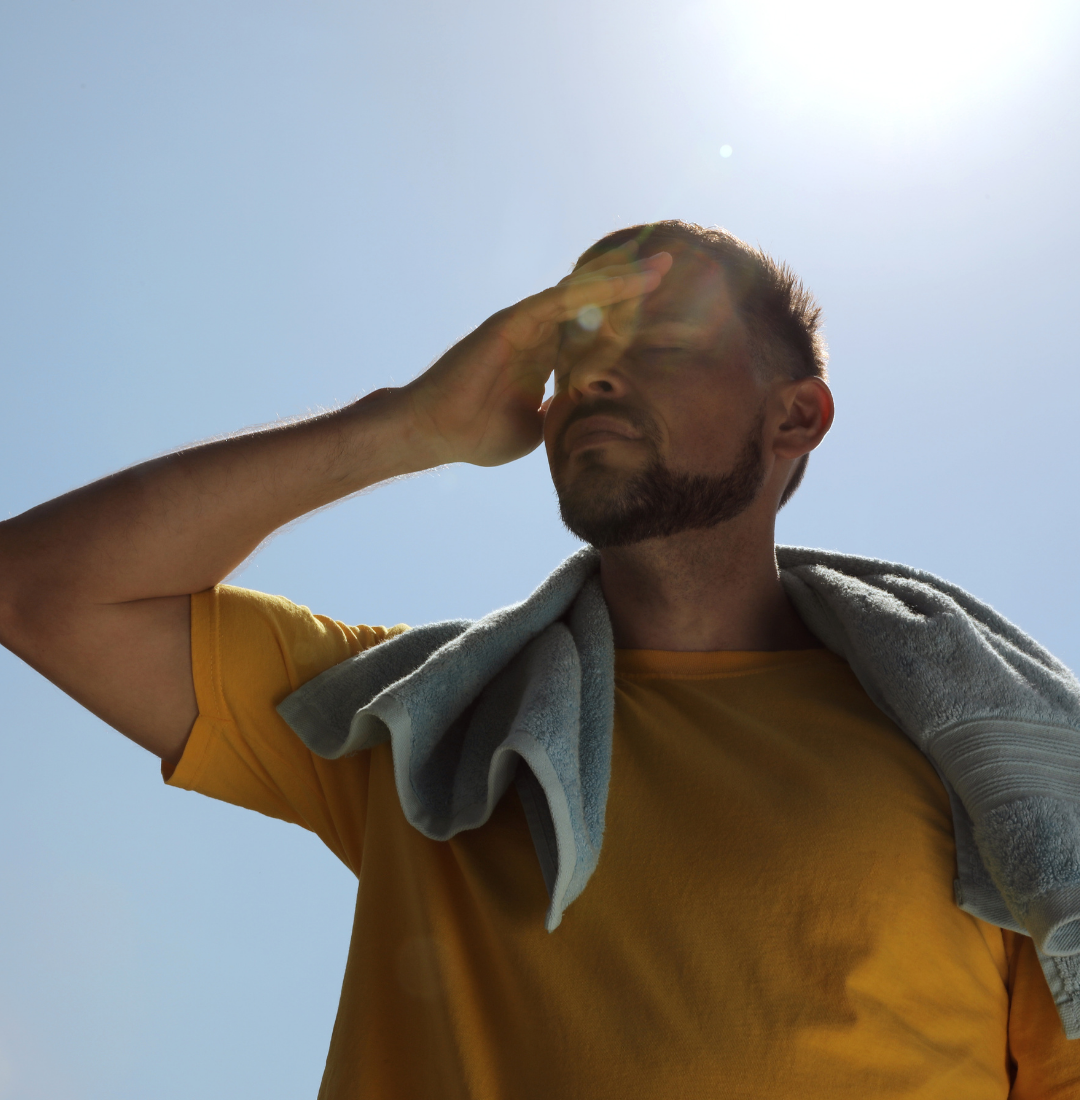 A person shielding their eyes from the sun with their hand, with a towel draped over their shoulders.