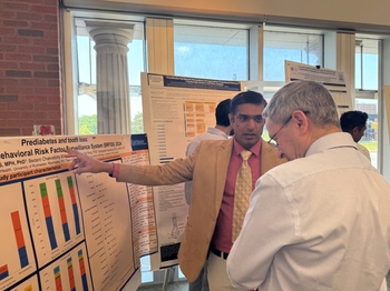 A young man points at a scientific poster titled "Prediabetes and tooth loss" as he speaks to a grey-haired gentleman.