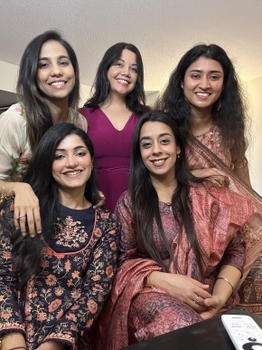 Five women pose together. They are all wearing pink or floral patterned outfits.
