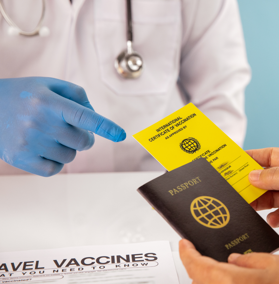 A gloved hand points to a yellow vaccination certificate held over a passport, with a document titled "TRAVEL VACCINES" visible in the foreground.