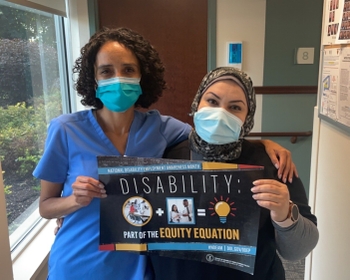 A woman with curly dark hair and a woman wearing a hijab hold up a sign together that reads "Disability: Part of the Equation"
