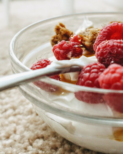 bowl of yogurt with a spoon and raspberries with granola 