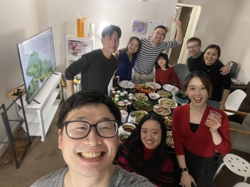 Nine people stand smiling around a table covered with platters of dumplings and other Chinese dishes.