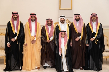 Six men and a young boy stand together, dressed in flowing robes and patterned head coverings.