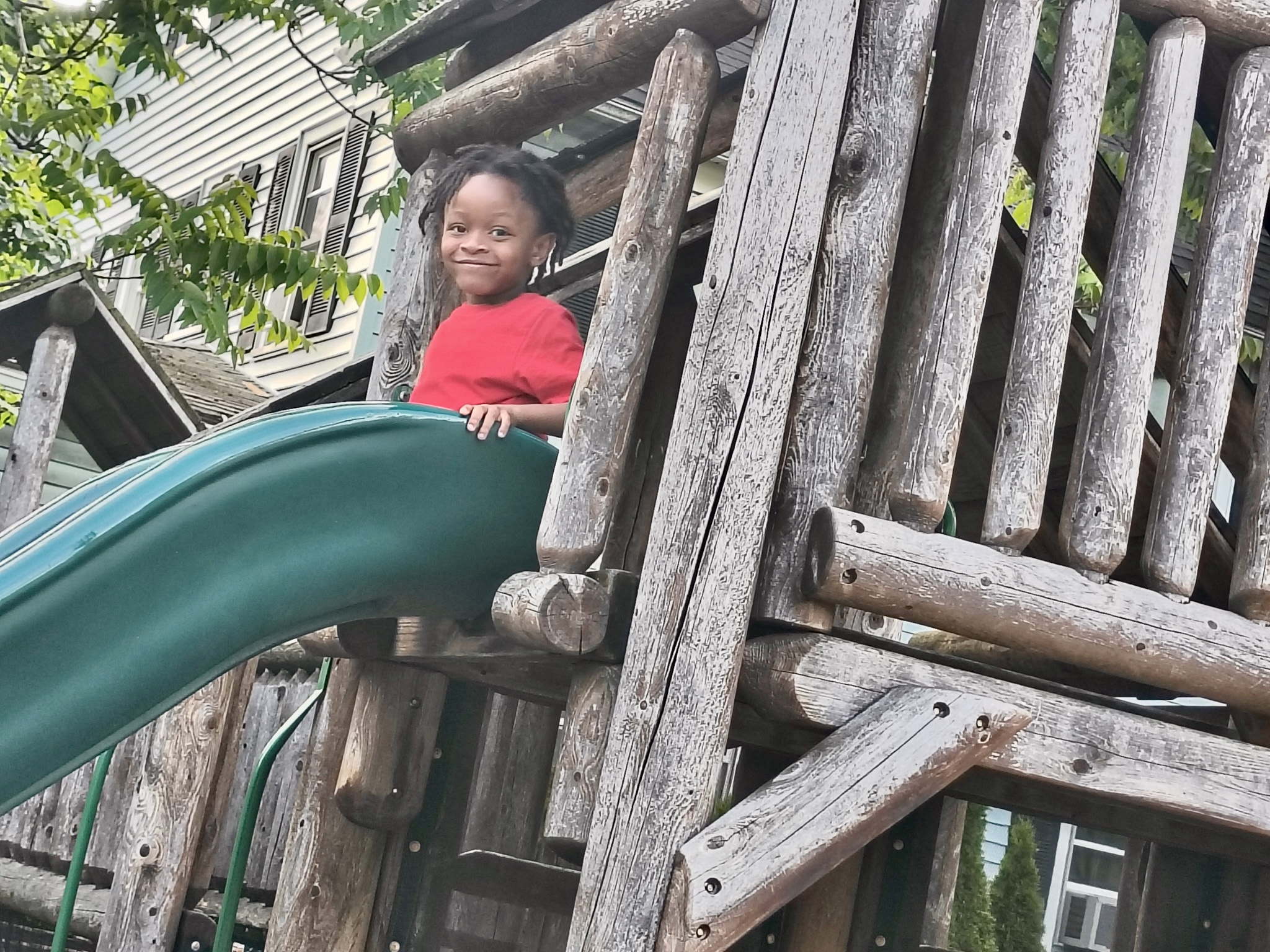 Child sitting at the top of a green slide on a playset