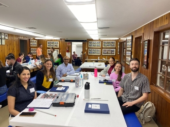 Six people look up and smile from their seats around a paper-covered table. On the table are several binders, boxes of tools, and dental models.