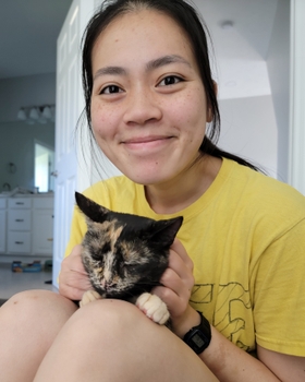 A woman sits on the floor hugging a speckled cat.