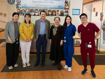 Six people of Chinese descent stand together smiling in the EIOH lobby. The two people on the right are wearing scrubs while the others are in semi-formal attire.