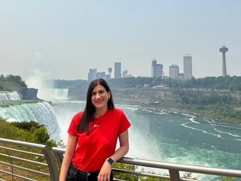 A young woman leans against a railing in front of Niagara Falls, a set of giant waterfalls.