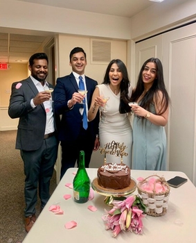 Two young men in suits and two young women in dresses share a happy toast in front of a cake decorated with the words "Our Happily Ever After"