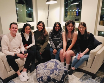Six people sit on a living room couch - 1 man and 5 women. 