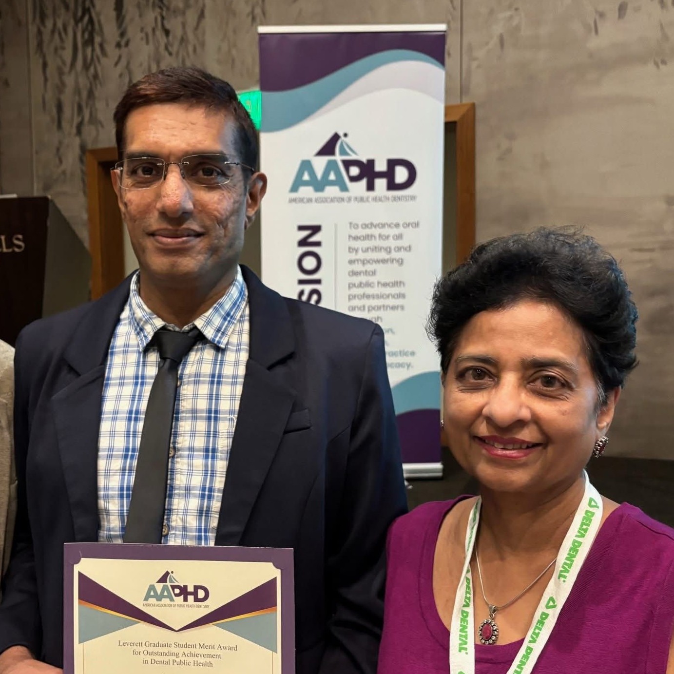 A young man holds a certificate, stands next to a shorter woman.