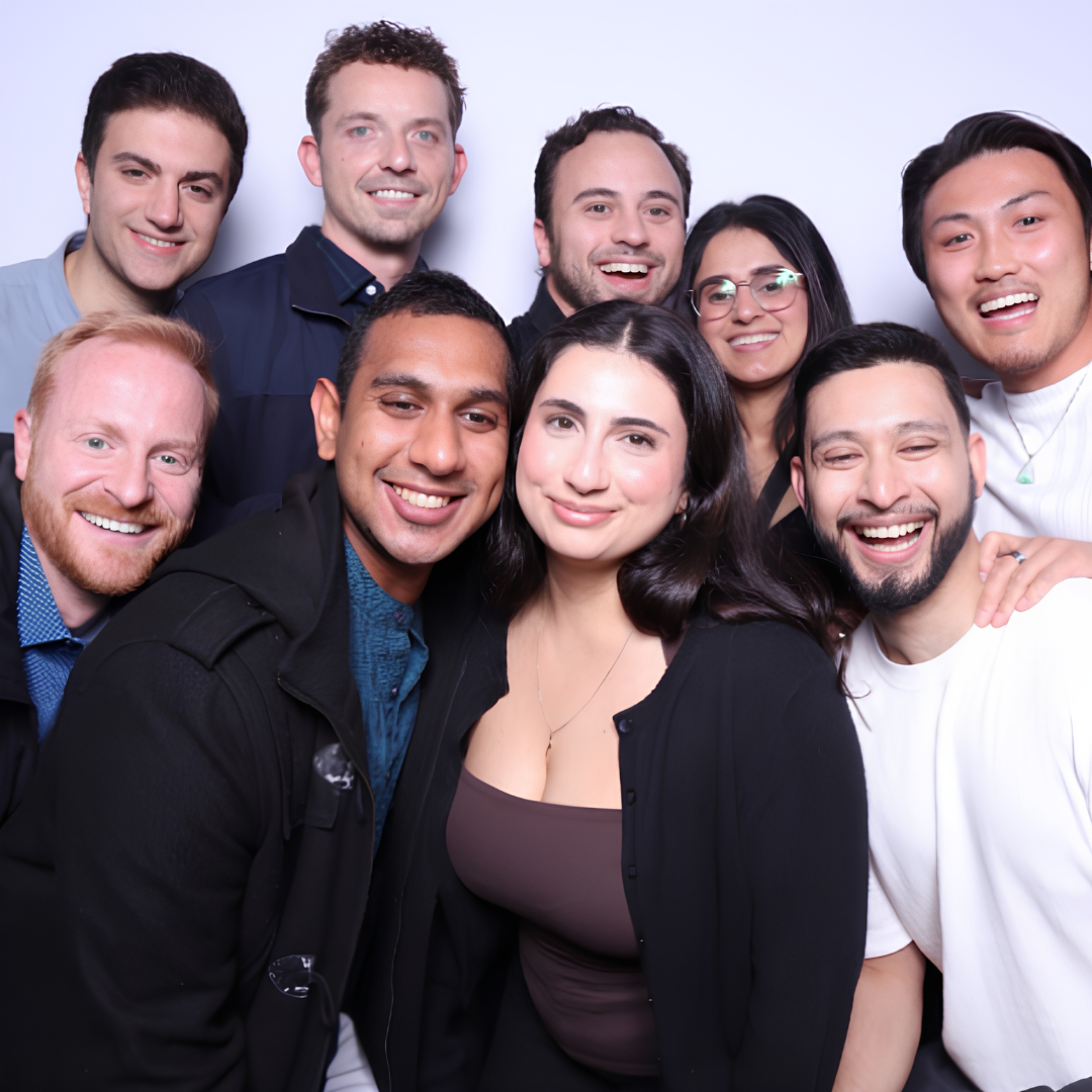 Nine people lean close together, smiling and laughing.