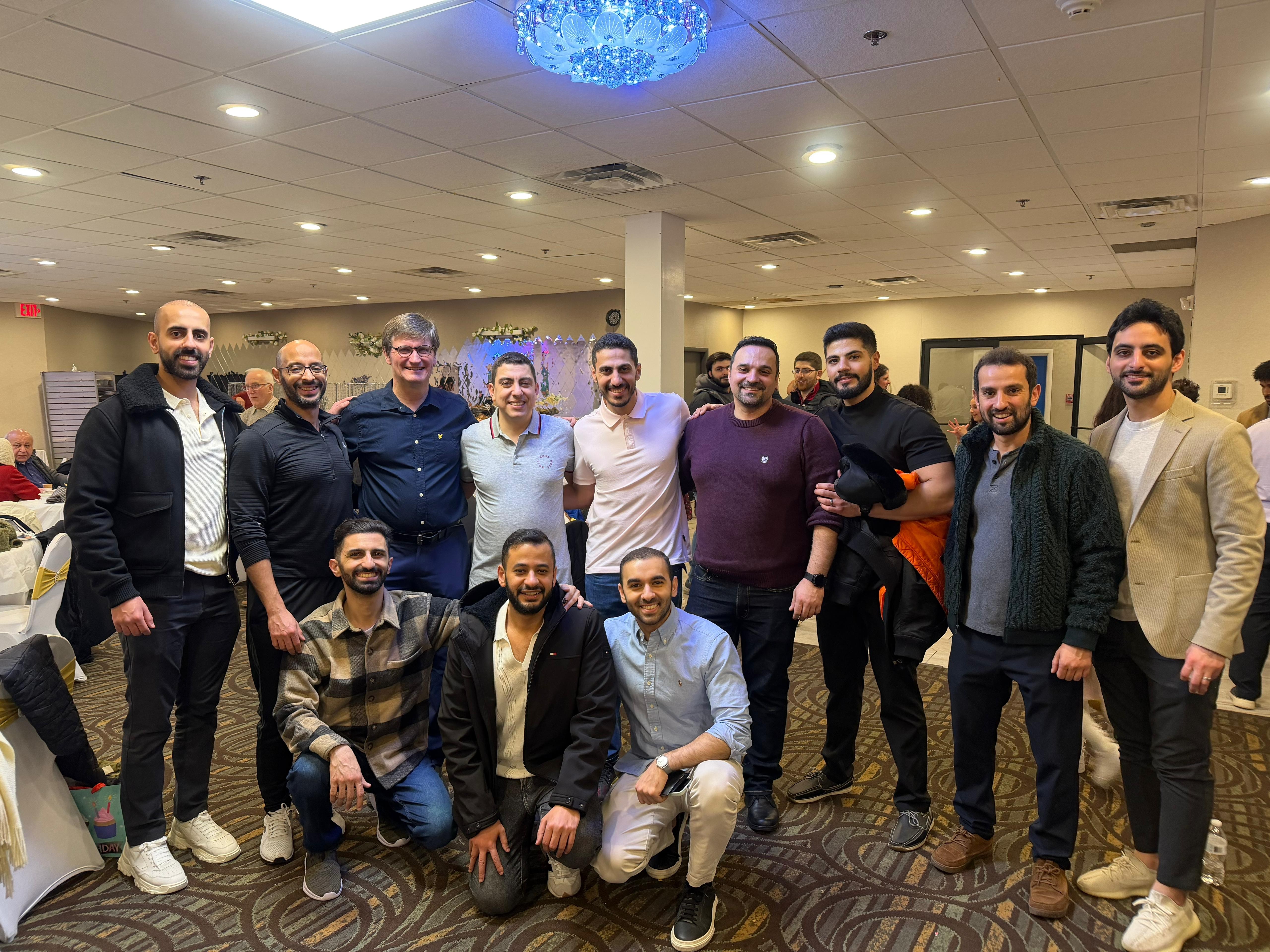 A group of men stands together smiling in a large room decorated for an event.