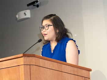 A woman with light brown skin and a bob of black hair speaks at a podium.