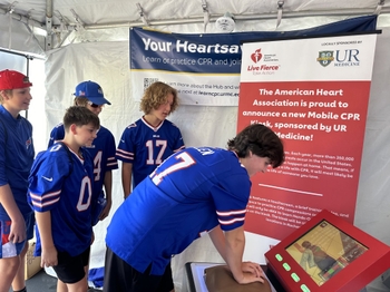 Friends watch a teen use the CPR training kiosk.