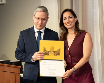 A woman with pale skin and dark brown hair accepts a certificate from a man with short grey hair.