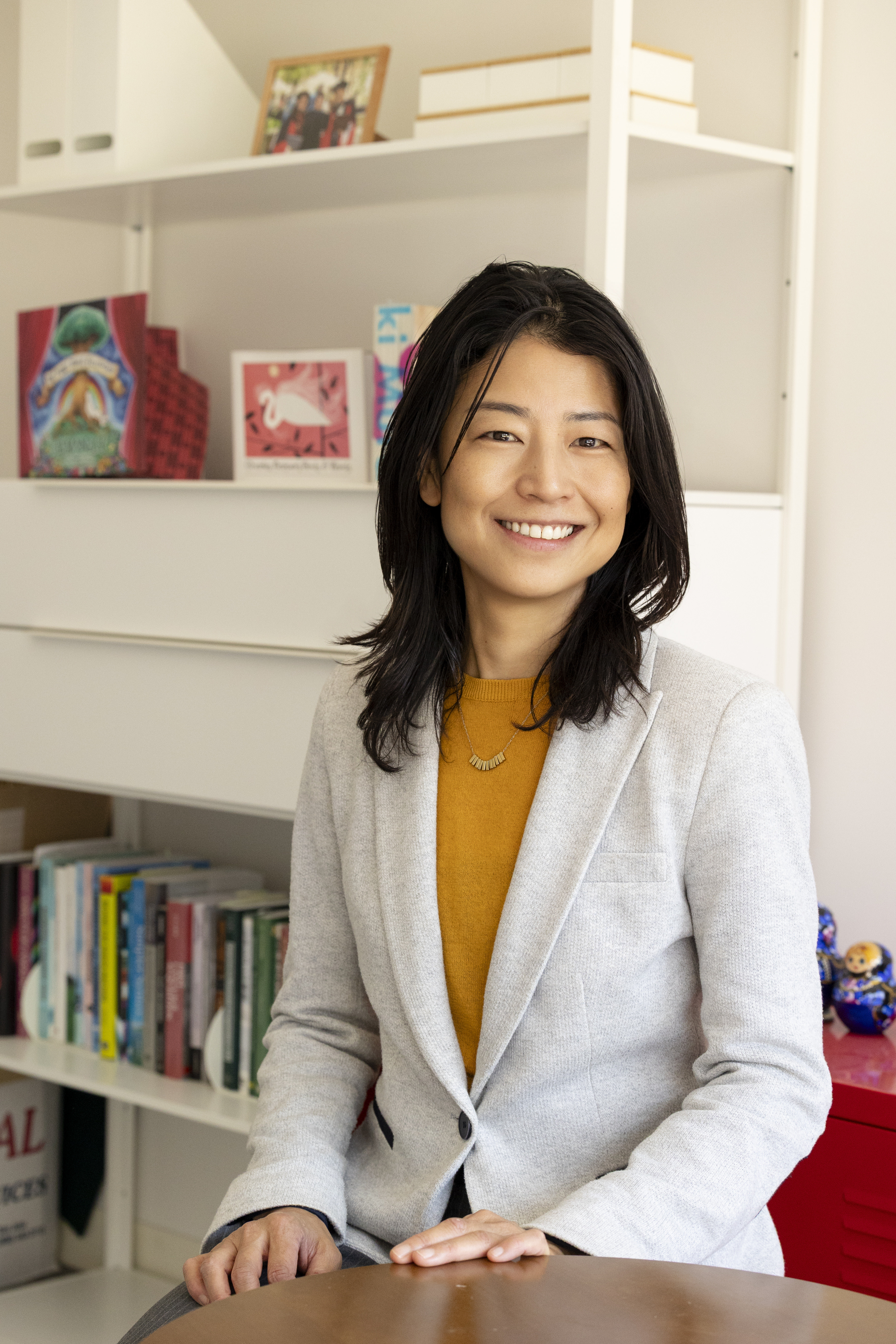 woman with shoulder length dark hair, wears a white blazer with a marigold colored shirt underneath
